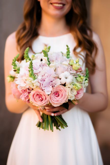 A floral bouquet featuring vibrant yellow gerbera daisies, white roses, and various shades of green foliage, arranged in a casual, rounded style. The flowers are fresh, with slightly textured petals a