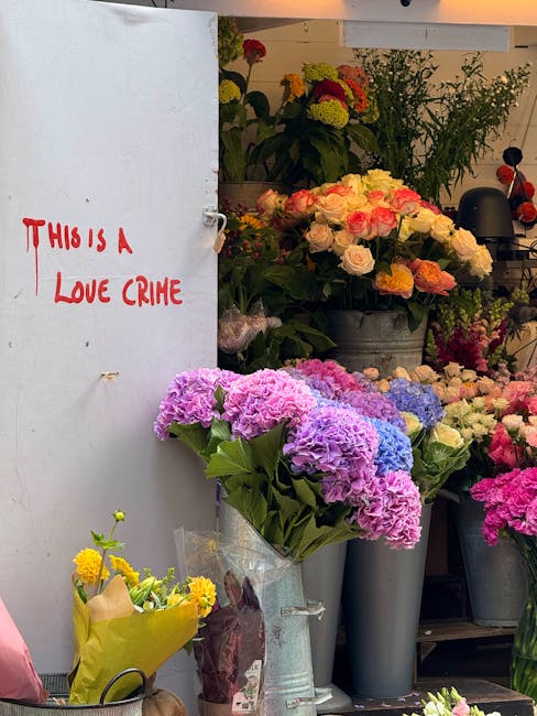 A vibrant outdoor floral display featuring an assortment of freshly-cut flowers arranged in brown paper wraps and placed in metal buckets and wooden crates. Prominent in the arrangement are bright yel