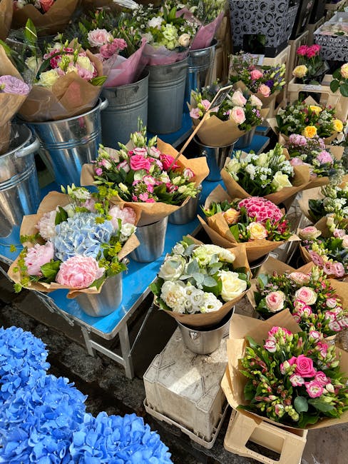 A vibrant display of fresh flower bouquets at a florist's stall, featuring a variety of tulips, roses, and small spray roses in shades of pink, red, purple, yellow, and white. The flowers are arranged