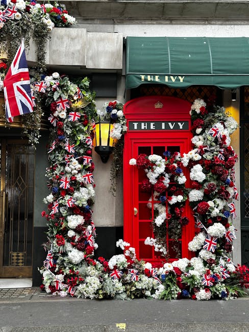 A vibrant floral display arranged around a classic red UK telephone box with the sign 'THE IVY,' decorated with a substantial arch and surround of white, red, and blue flowers, including chrysanthemum